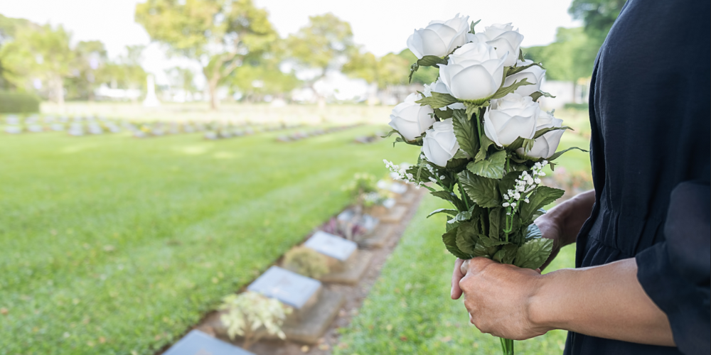 Femme en deuil tenant des fleurs blanches dans un cimetière.