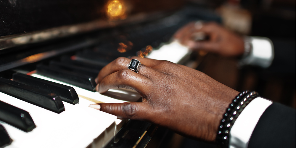 Close-up of hands playing piano against a dark background.