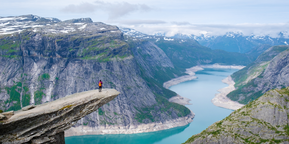 Un randonneur se tenant debout au bord de l’éperon rocheux de Trolltunga, en Norvège.