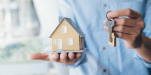 A man holding a model house and a key.