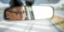 Plan rapproché d’un homme âgé vu dans le rétroviseur de sa voiture. 